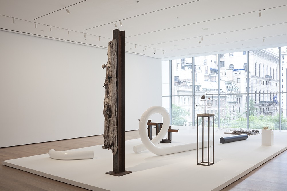 View of several sculptures, including a vertical I-bean and a looping white-painted steel piece, resting on a large white platform