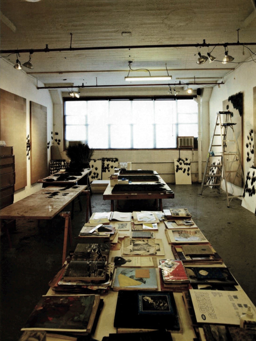 A view of Carol Bove's studio featuring a long table laden with books in the foreground.