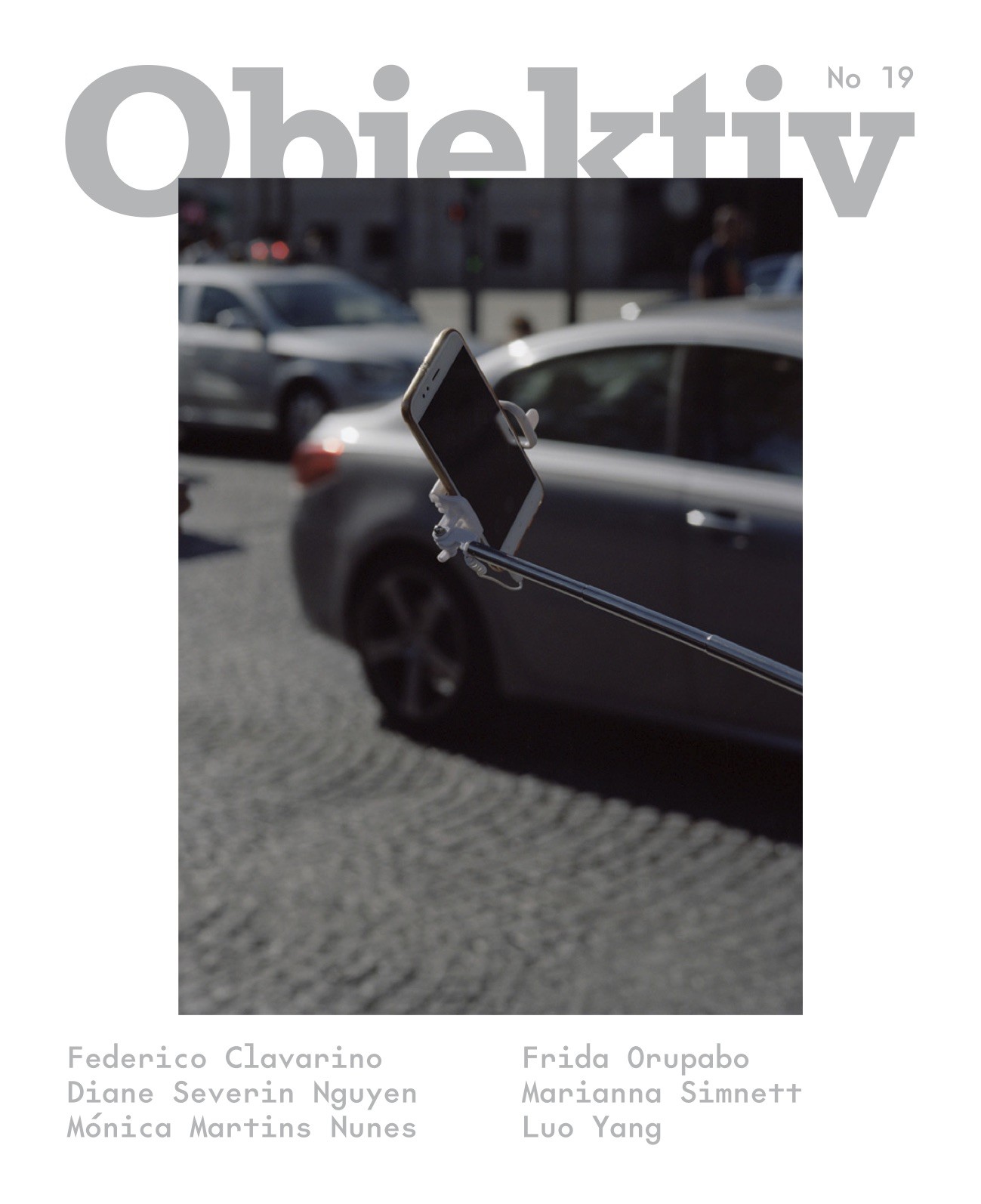 The cover of _Objektiv_ 19, featuring a photograph by Federico Clavarino. The picture depicts a cell phone held by a selfie stick next to a busy urban road.