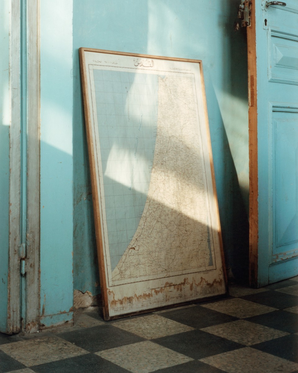 An image of a framed map, with Arabic writing, leaning against a teal-colored wall in a somewhat rundown interior.
