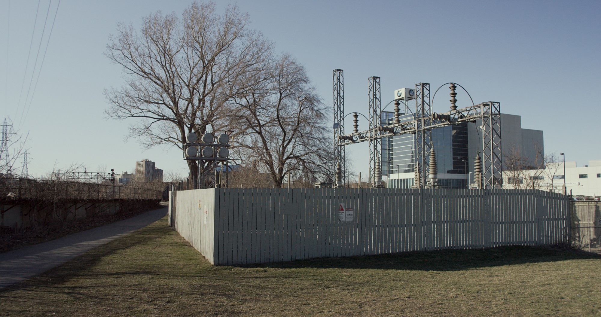A still from Mark Lewis's 2017 film Valley depicting electrical power equipment behind a gray-painted wooden fence.