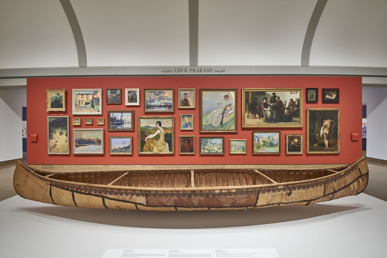 A view of the new Canadian and Indigenous art galleries at the National Gallery of Canada, Ottawa. The photo includes an Indigenous-made canoe and a wall hung salon-style with landscape and portrait paintings.