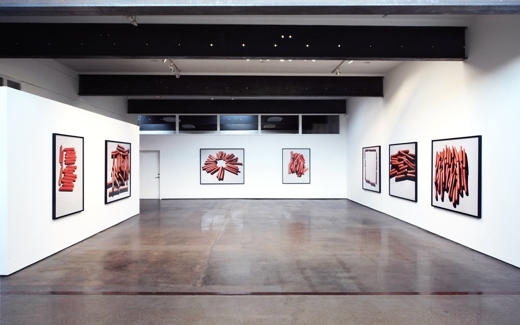 A view of a gallery interior with seven large framed photographs of hot dogs.