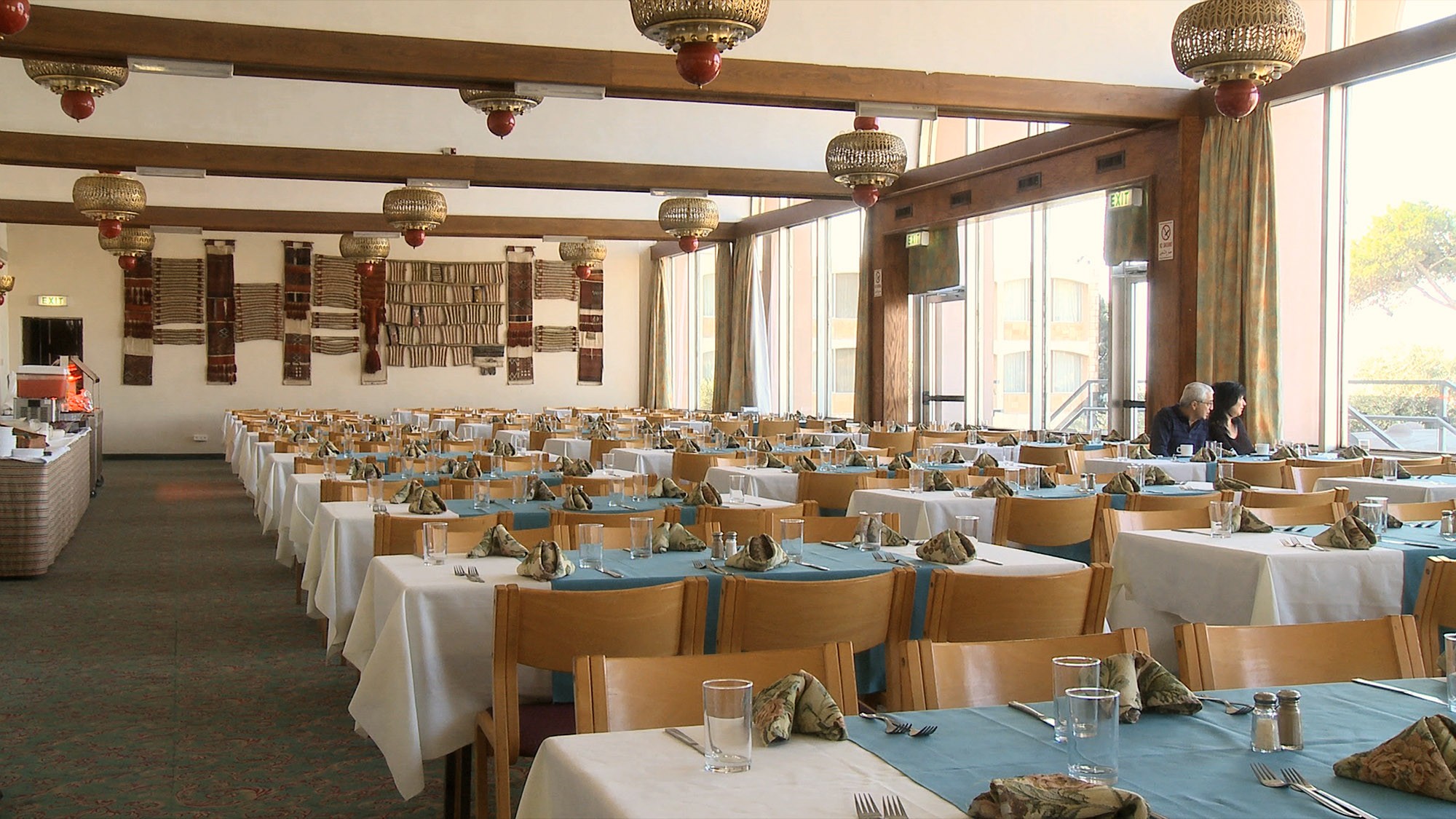 This image, from Nir Evron's 2009 film Oriental Arch, depicts two people sitting side-by-side near the window in an oversize hotel dining room.